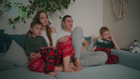 Caucasian-family-sitting-together-on-a-sofa-and-watching-TV-at-home-during-Christmas-holidays-decorated-apartment-interior.-High-quality-4k-footage